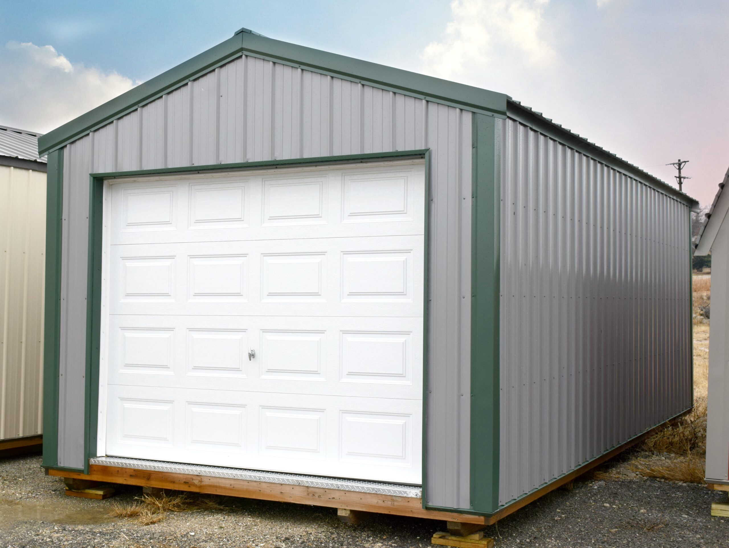 Gray metal garage with white door and green trim and roof