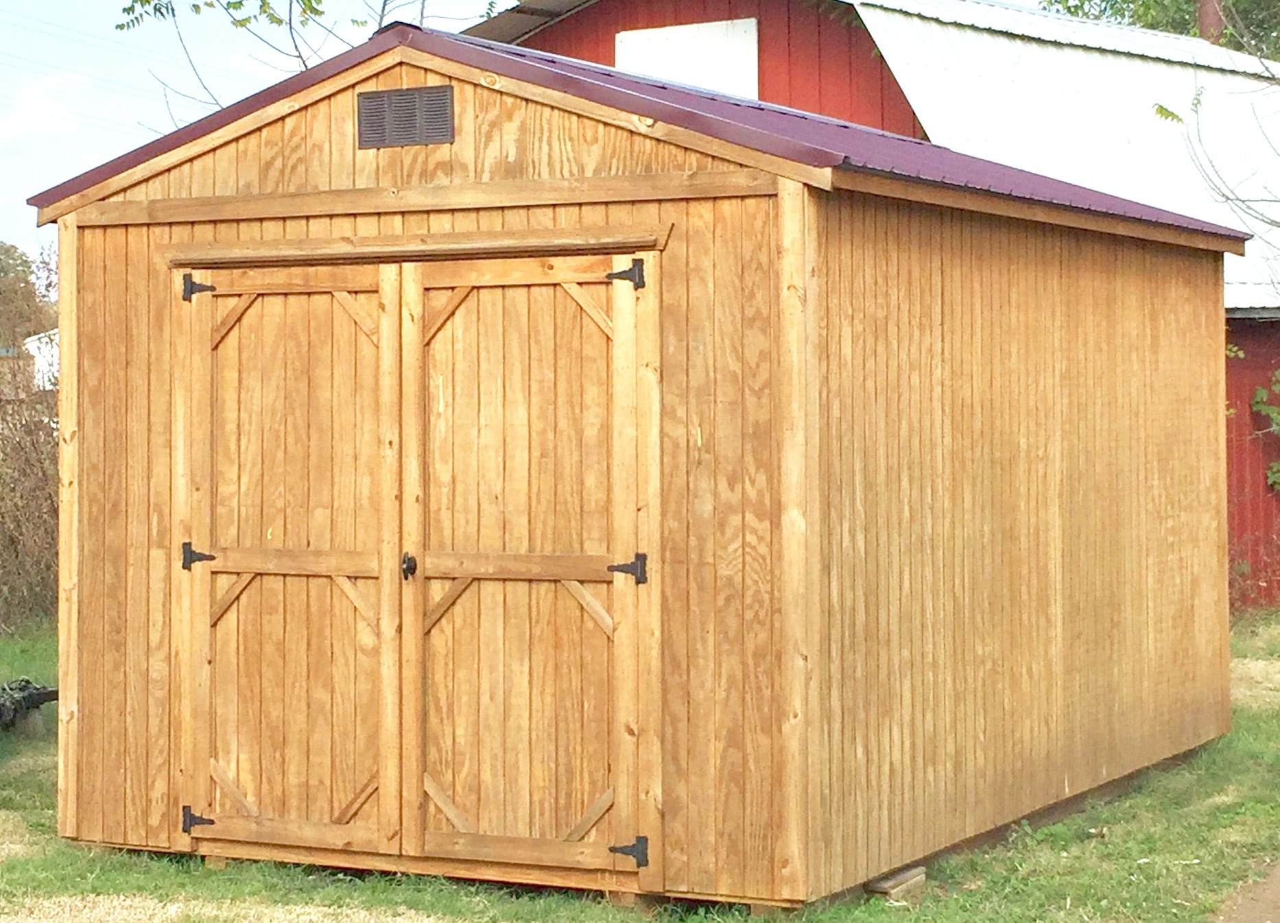 Light wood treated utility shed with burgundy metal roof